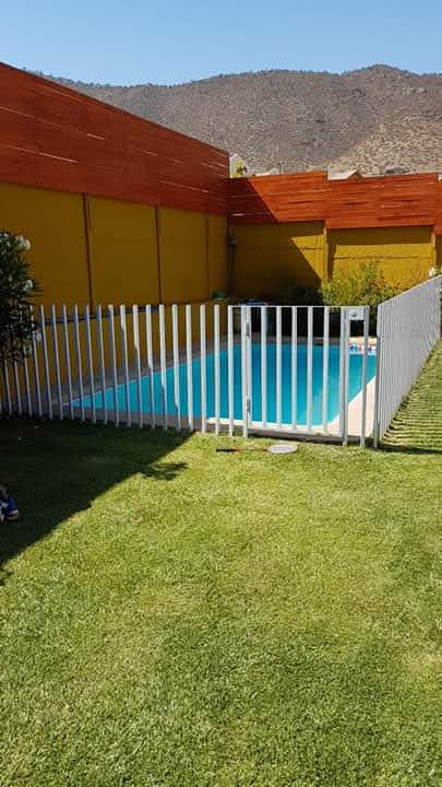 Reja blanca cerrando el perímetro completo de una piscina, con portón